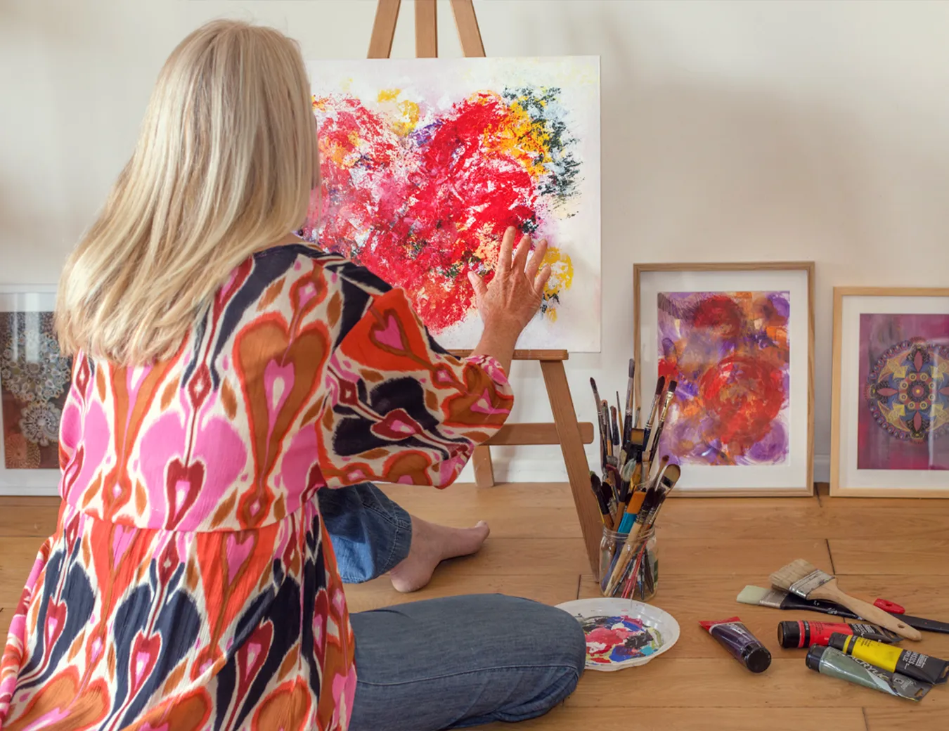 Maria José Martinez peignant une œuvre sur mesure dans son atelier, assise au sol devant son chevalet.