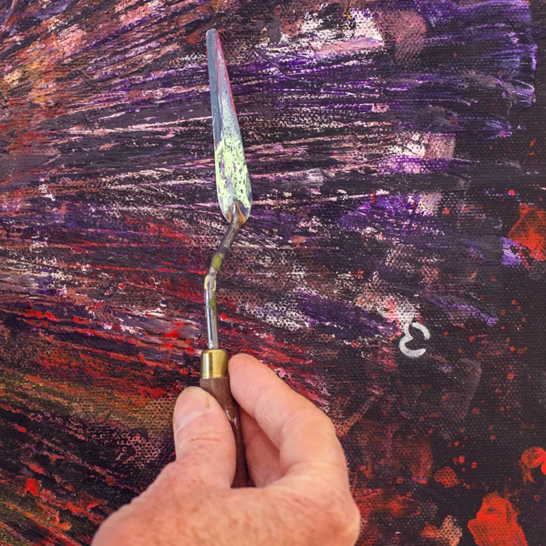 Main de Maria José Martinez appliquant la peinture au couteau sur une œuvre originale abstraite.